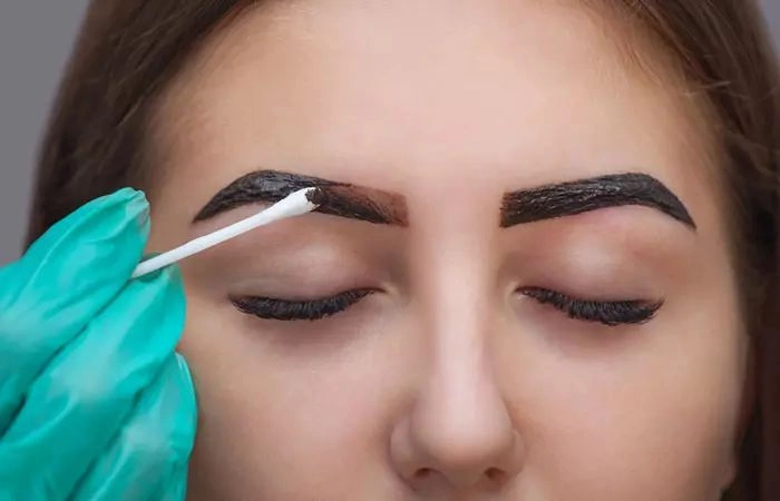 Esthetician using a clean cotton swab for precise eyebrow tint cleanup
