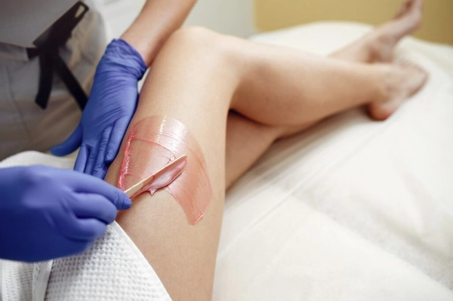 Professional esthetician applying wax with spatula during Brazilian CBD waxing session